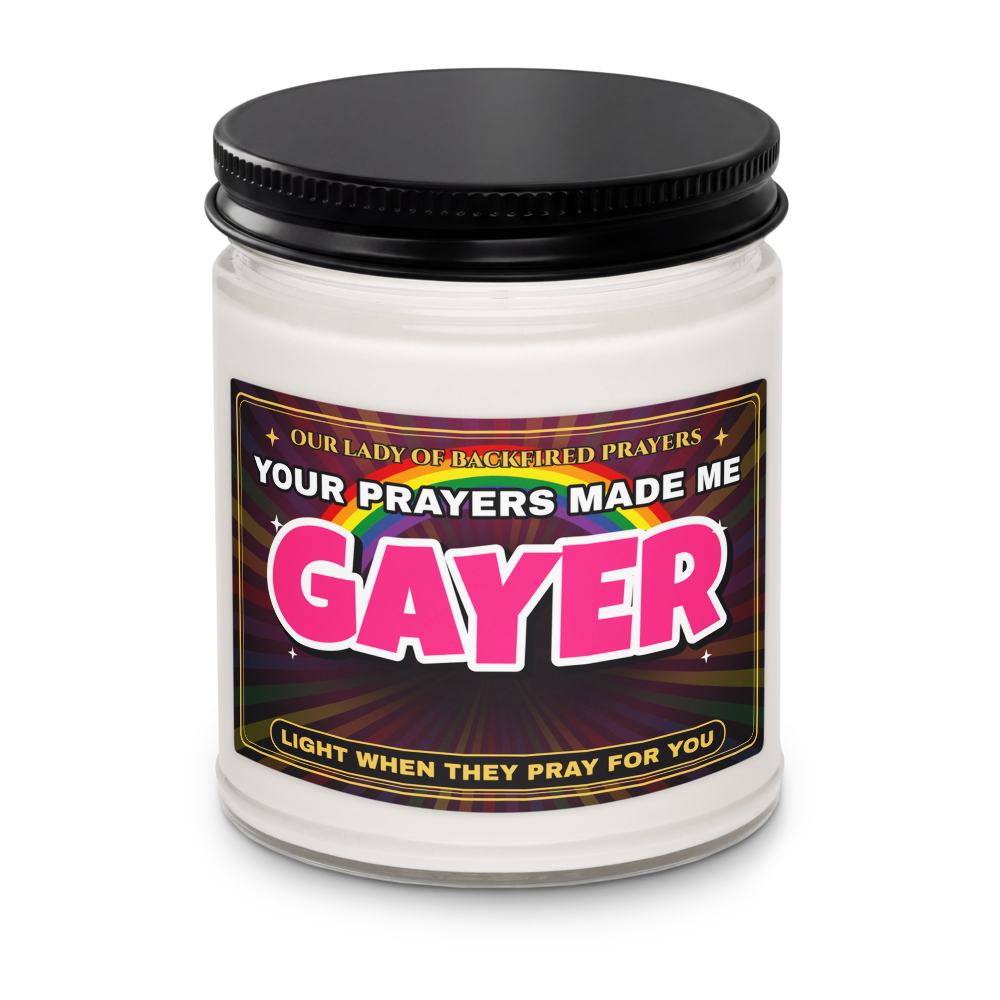 Close-up of the Nice Gay soy candle with its black lid on, showing the label reading "Our Lady of Backfired Prayers," "Your Prayers Made Me GAYER," and "Light when they pray for you."
