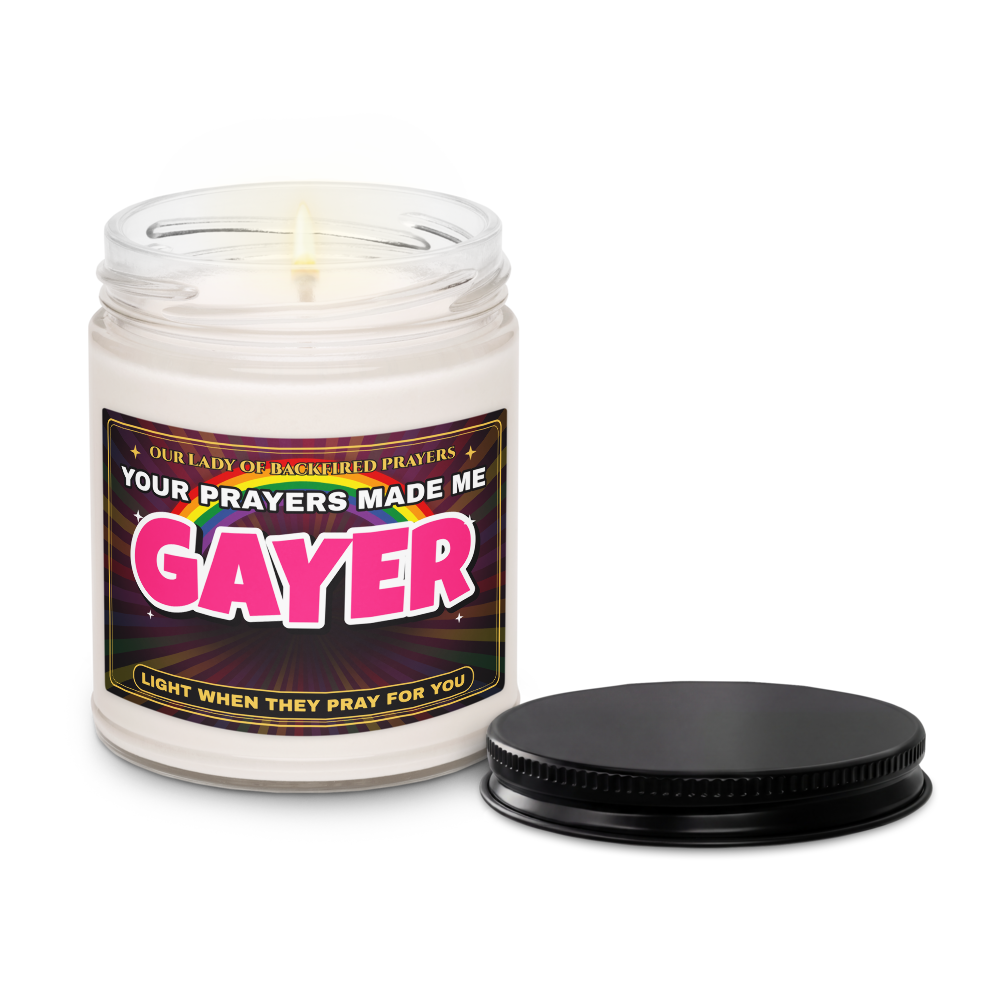Lit Nice Gay soy candle with the lid off beside its black lid, label reading "Our Lady of Backfired Prayers" and "Your Prayers Made Me GAYER."